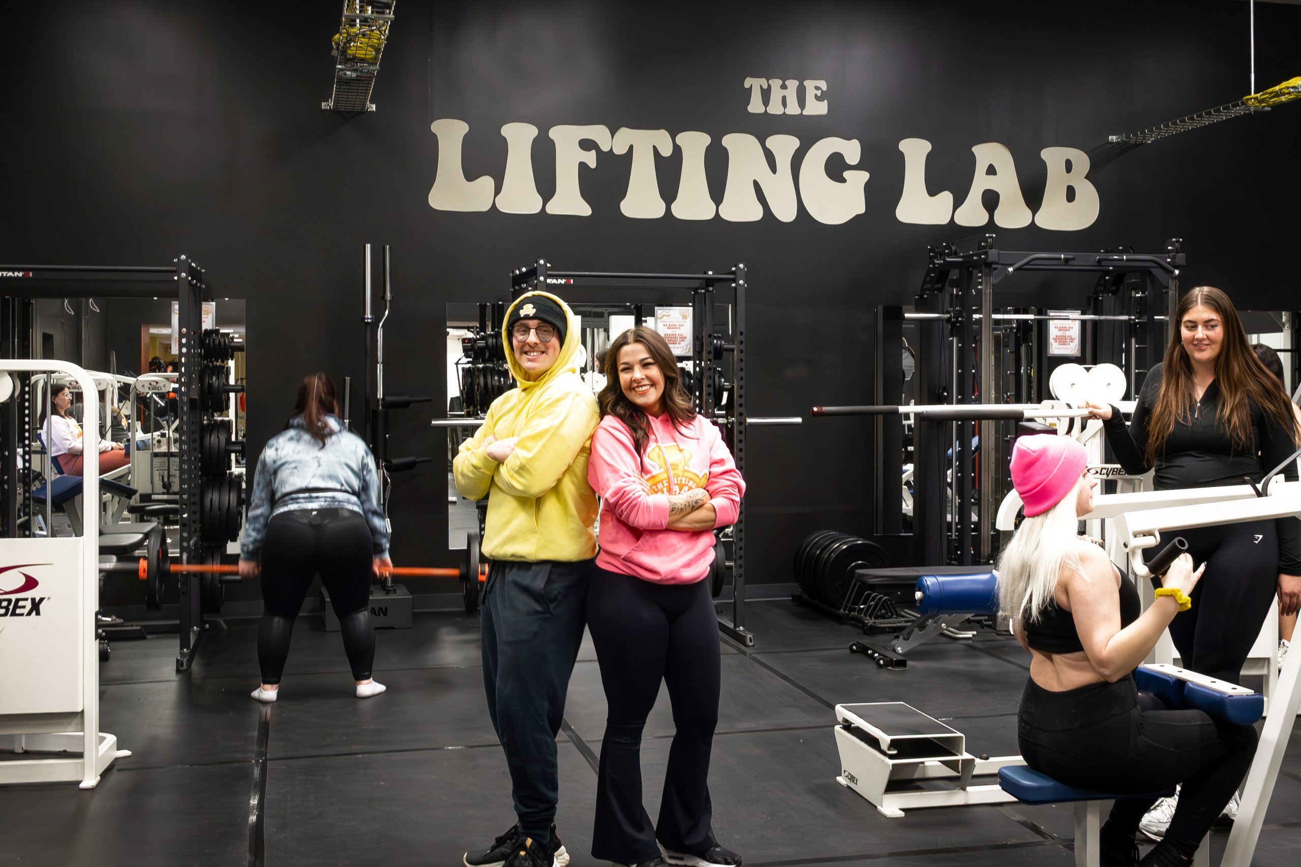Anna & Caden standing in the gym surrounded by members working out